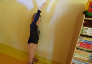 Dziewczynka stoi pod ścianą i z ręki tworzy cień na ścianie.